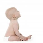 Baby Junge sitzend und aufblickend auf weißem Hintergrund, Seitenansicht. — Stockfoto