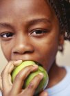 Elementary age boy taking bite of green apple, portrait. — Stock Photo