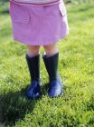 Toddler girl in rubber boots on green meadow. — Stock Photo