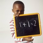 Garçon de l'âge primaire tenant tableau noir avec équation arithmétique . — Photo de stock