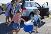 Семья с двумя детьми распаковывает машину и несет корзину для пикника . — стоковое фото