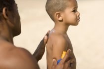 Чоловік розбризкує сонячний крем на сина на пляжі . — стокове фото