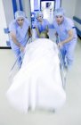 Squadra di emergenza spingendo barella ospedaliera con paziente in corridoio
. — Foto stock