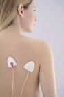 Jeune femme utilisant une stimulation nerveuse électrique transcutanée sur le dos . — Photo de stock