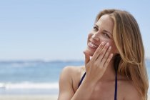 Femme appliquant de la crème solaire sur la plage. — Photo de stock