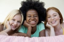 Three cheerful teenage girls hanging out on bed indoors. — Stock Photo