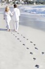 Älteres Paar spaziert mit Fußabdrücken auf Sand am Strand. — Stockfoto