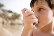 Asthmatic boy using inhaler at beach. — Stock Photo