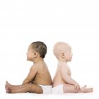 Bébé fille et bébé garçon assis dos à dos sur fond blanc . — Photo de stock