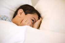 Little boy playfully hiding face in bed. — Stock Photo
