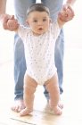 Infant baby boy being supported by father on floor. — Stock Photo