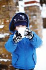 Elementary age boy in winter clothing holding snowball on street. — Stock Photo