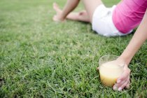 Жінка сидить на траві зі склянкою фруктового соку . — стокове фото