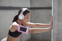Woman wearing headphones and stretching against wall — Stock Photo