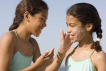 Girl applying sun cream to sister face. — Stock Photo