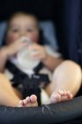Close-up de pés de bebê menino bebendo garrafa de leite enquanto amarrado em cadeira de segurança . — Fotografia de Stock