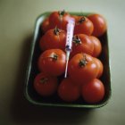 Pomodori geneticamente modificati con siringa su vassoio . — Foto stock
