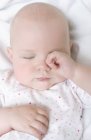 Infant baby rubbing eye in bed. — Stock Photo