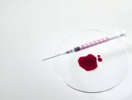 Pool of blood in watch glass with syringe. — Stock Photo