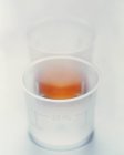 Due bicchieri di plastica, uno contenente medicina liquida . — Foto stock