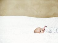 Infant baby in pajamas lying down on bed and looking in camera. — Stock Photo