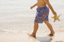Boy walking along beach and holding starfish. — Stock Photo
