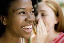 Teenage ginger girl whispering with female afro-caribbean friend. — Stock Photo