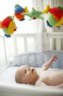 Infant baby boy lying in cot and looking up at toys. — Stock Photo