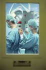 Krankenschwester hilft Chirurg und bindet Schutzkleidung hinter Tür. — Stockfoto