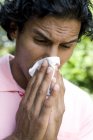 Man sneezing into handkerchief outdoors. — Stock Photo