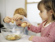 Preschooler children cracking eggs into mixing bowl. — Stock Photo
