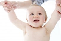 Bébé debout les bras levés soutenu par un parent . — Photo de stock