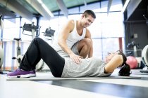 Junger Mann hilft Seniorin beim Turnen im Fitnessstudio. — Stockfoto