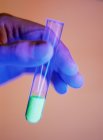 Wissenschaftler Hand hält Reagenzglas mit festen fluoreszierenden chemischen glühend grün. — Stockfoto