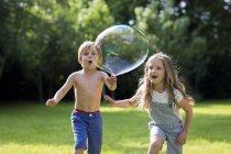 Брат и сестра гоняются за пузырьком в саду . — стоковое фото