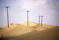 Pylons de madeira apoiando linhas elétricas através de dunas de areia em Emirados Árabes Unidos . — Fotografia de Stock