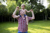 Father carrying son on shoulders in garden. — Stock Photo