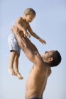 Отец поднимает сына против голубого неба на пляже . — стоковое фото