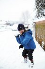 Junge im Grundschulalter in Winterkleidung spielt auf Straße mit Schneeball. — Stockfoto