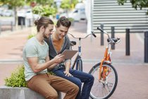 Hombres jóvenes sentados en la pared de la calle con tableta digital . - foto de stock