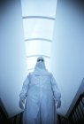 Vista frontal del científico masculino en traje de aislamiento blanco en pasillo . - foto de stock