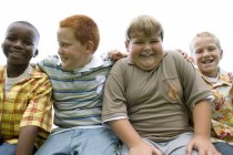 Portrait of group of elementary age boys sitting side by side outdoors. — Stock Photo