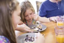 Children eating blueberry pancakes at dining table. — Stock Photo