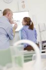 Male dentist holding X-ray against lightbox and showing to girl. — Stock Photo