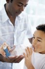 Father helping asthmatic son using spacer inhaler with plastic chamber. — Stock Photo