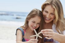 Mother with daughter holding starfish on beach. — Stock Photo