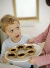 Sister offering brother freshly baked jam tarts on plate. — Stock Photo