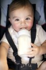 Bambino bambino beve bottiglia di latte mentre è legato sulla sedia di sicurezza . — Foto stock