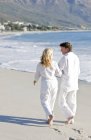 Зрелая пара, идущая рука об руку на песчаном пляже . — стоковое фото