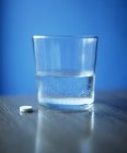 Таблетки біля склянки води на столі . — стокове фото